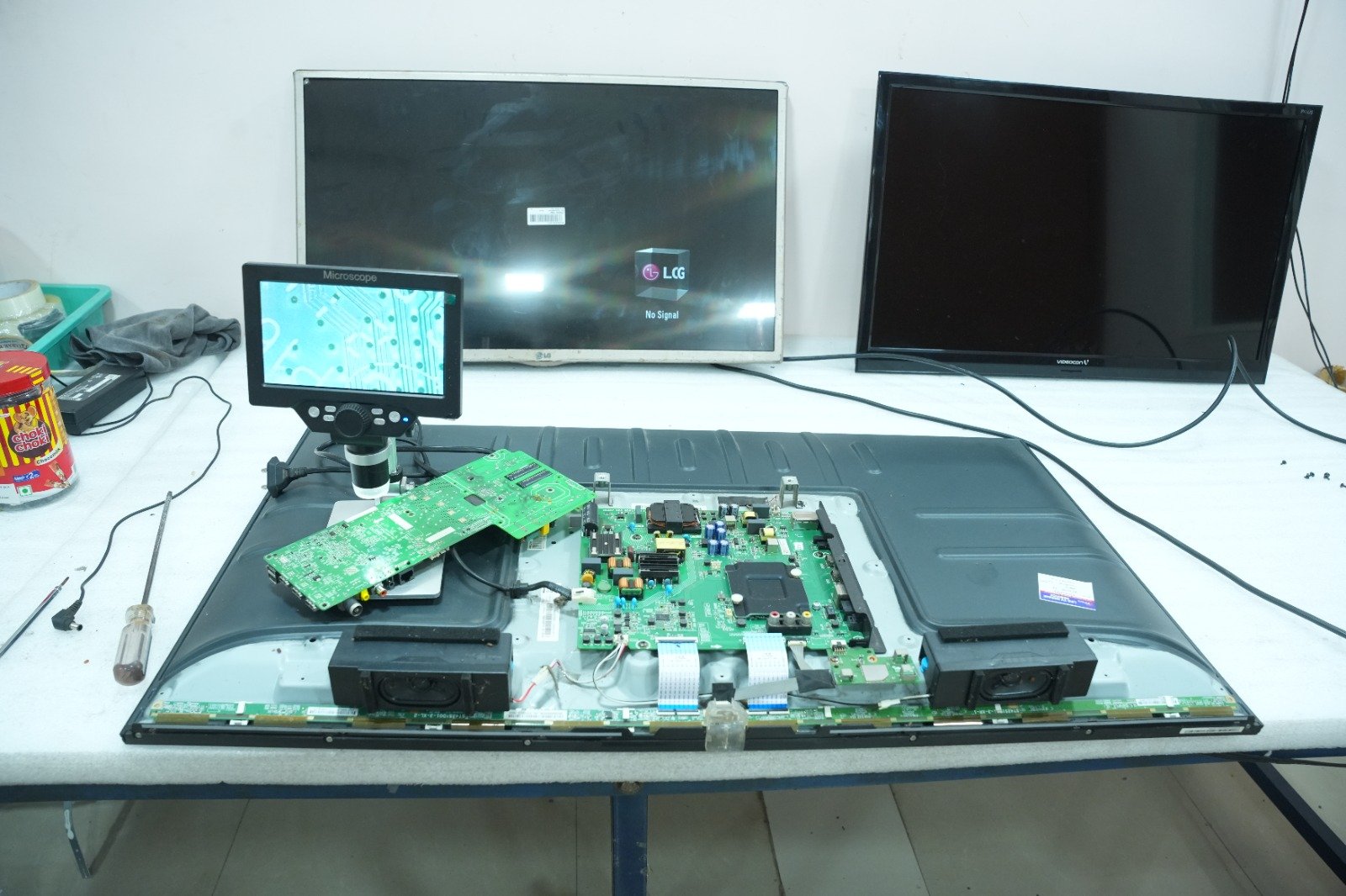 TV repair workbench in Visakhapatnam with an opened LED TV panel, main board and inspection microscope